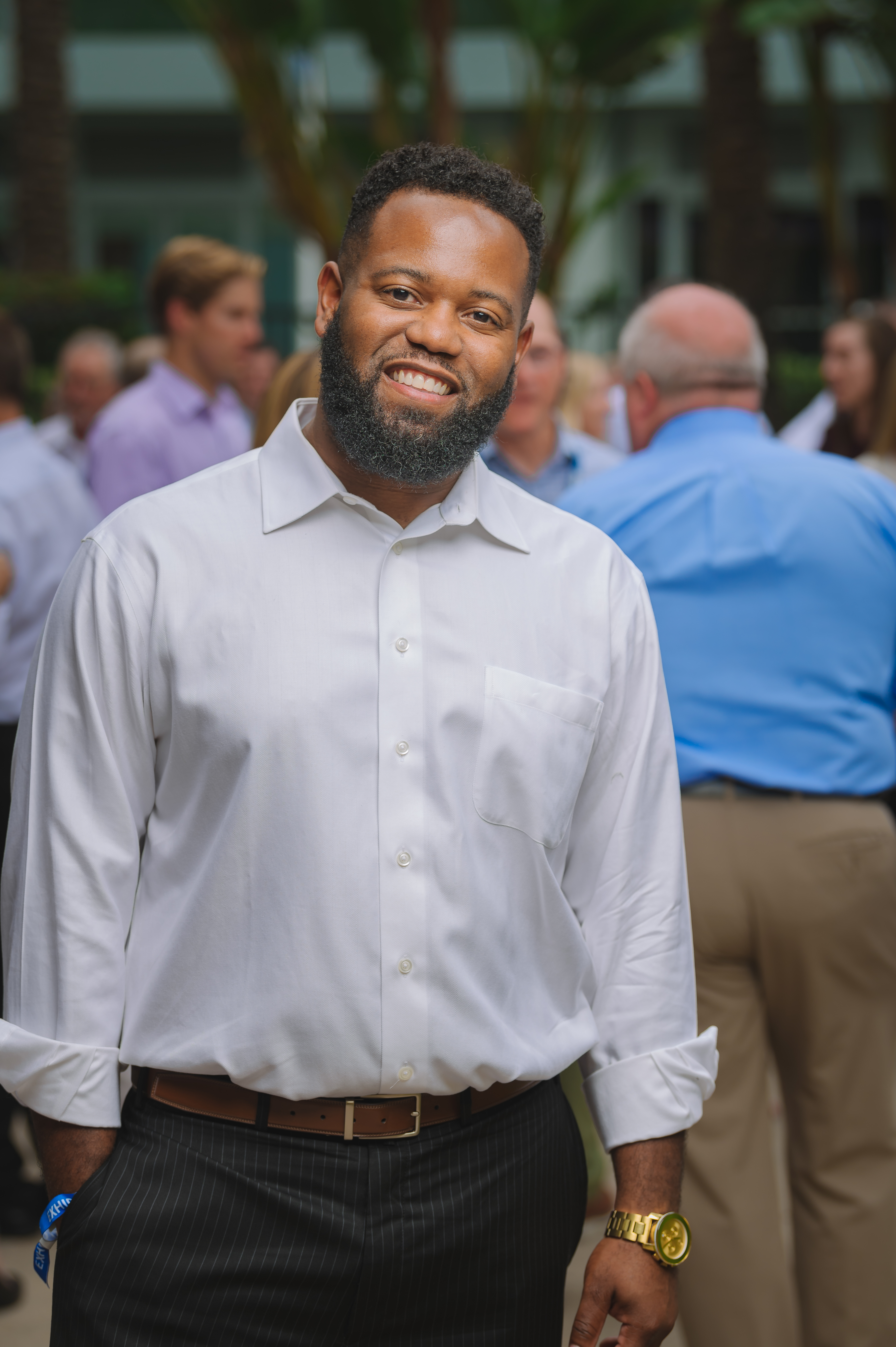 Man smiling in front of a crowd of people wearing a white shirt and black pants