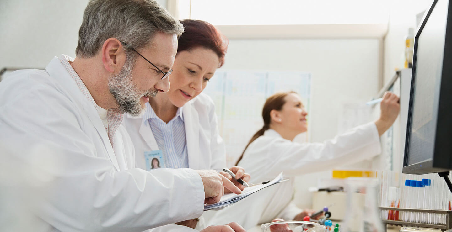 A male and female doctor look over a medical file with a third doctor in the background