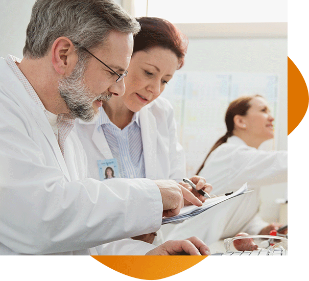 A male and female doctor look over a medical file with a third doctor in the background