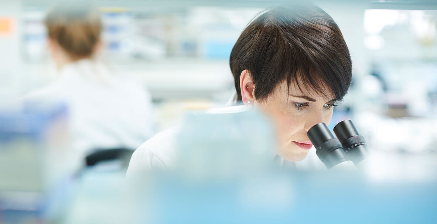 A banner image of a female Millar scientist looking through a microscope