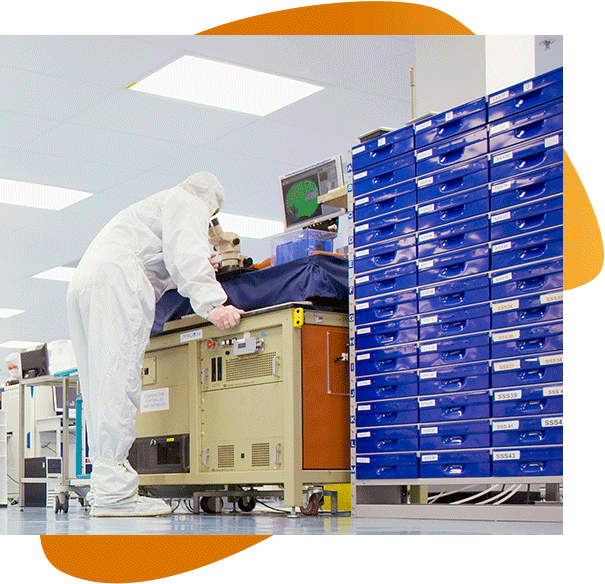 A millar scientist in full scrubs looking into a microscope by blue containers on a rack